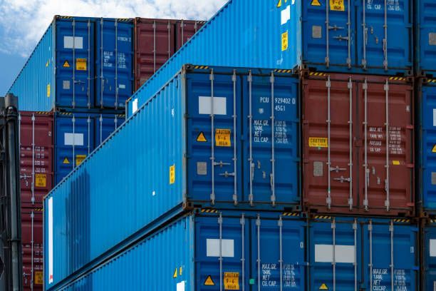 Blue and red shipping containers stacked at a port, blue sky in the background.
