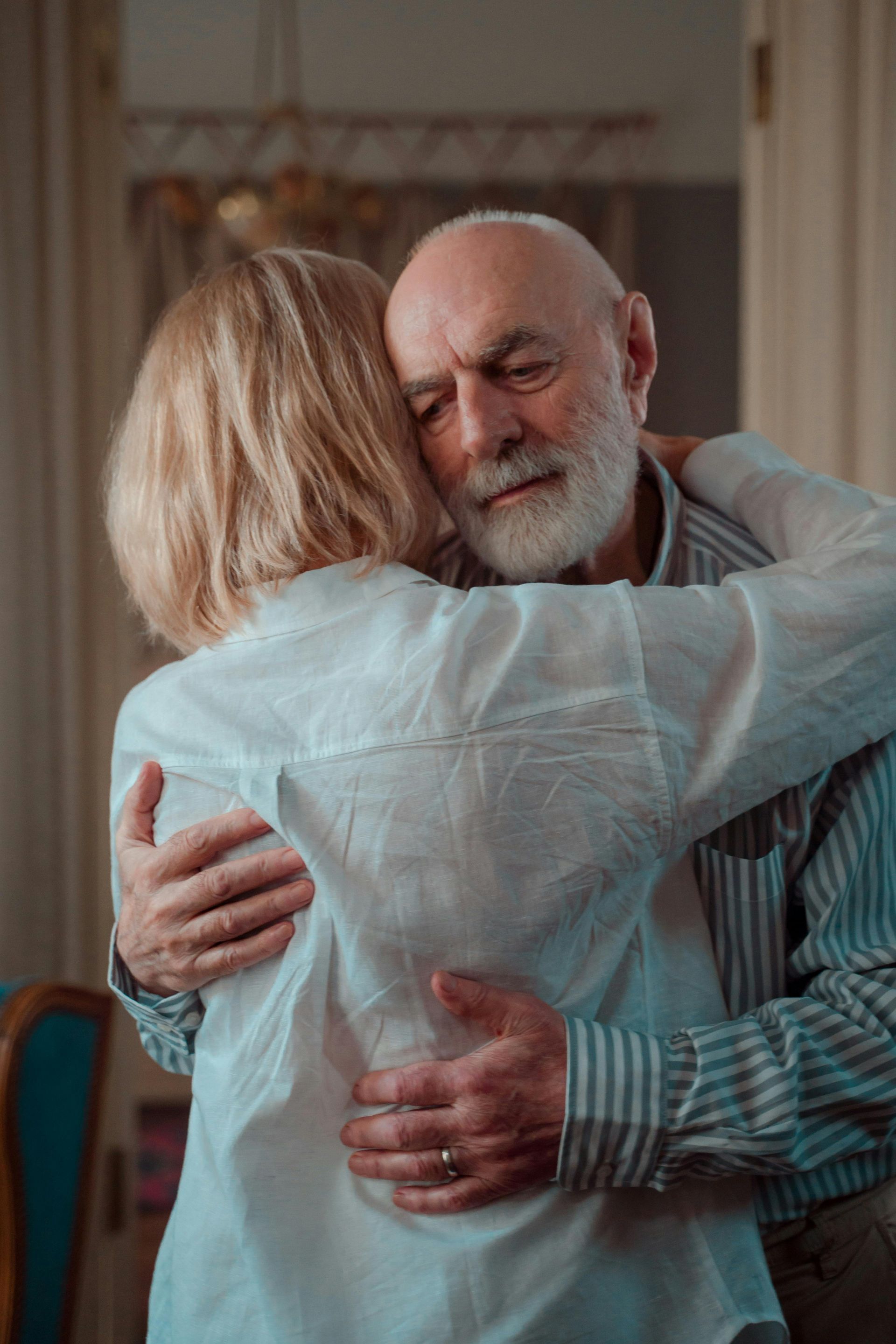 Two people embracing indoors, with one person’s back to the camera and the other smiling gently.