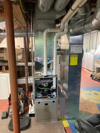 Furnace in a basement with vent pipes. Grey metal, white plastic, and yellow energy sticker.