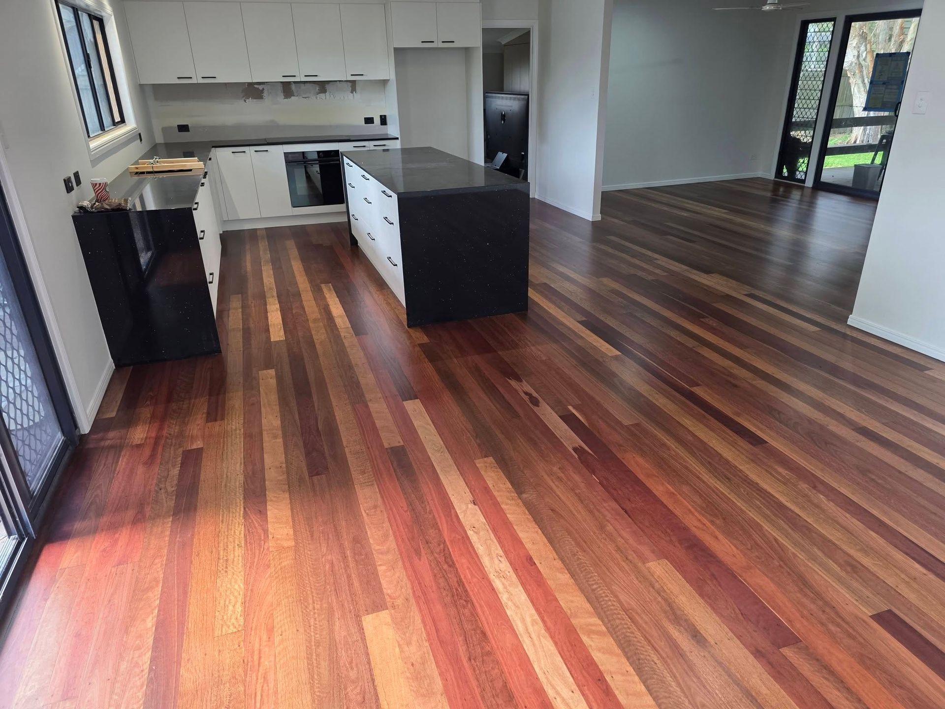 Kitchen with hardwood floors, white cabinets, black island, and access to a dining area — Alan Aldridge Floor Sanding in Urraween, QLD