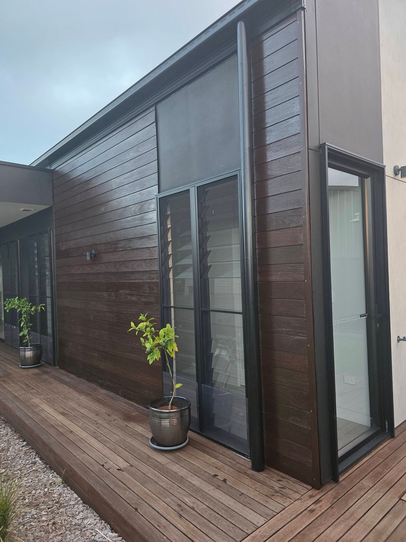Wooden-clad building with glass door, black frames. Wooden deck with potted plants. Cloudy day — Alan Aldridge Floor Sanding in Urraween, QLD