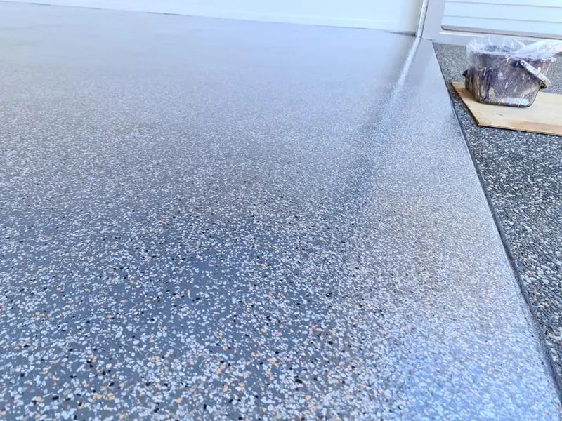 A Close Up of a Gray Concrete Floor With a Broom in the Background — Alan Aldridge Floor Sanding in Maryborough, QLD