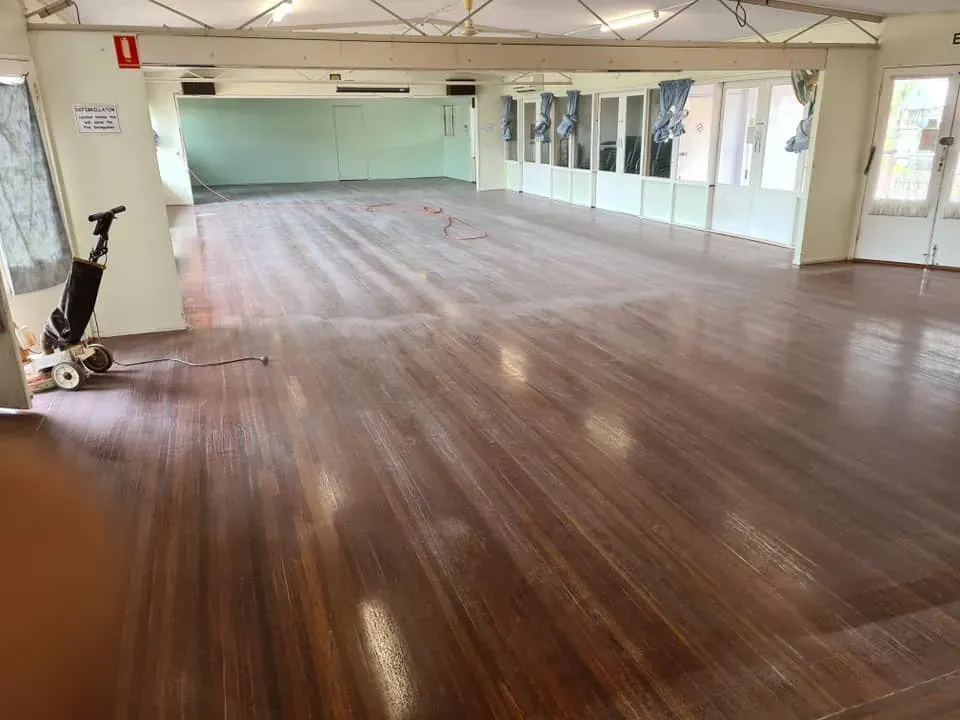 A Large Empty Room With a Wooden Floor and a Vacuum Cleaner — Alan Aldridge Floor Sanding in Urraween, QLD