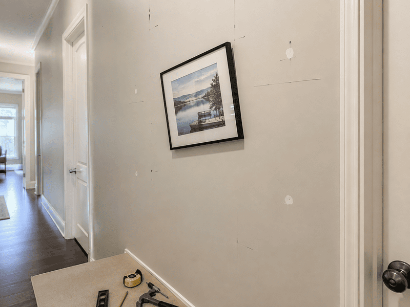 Hallway with a tilted framed picture on a beige wall and tools on the floor near the baseboard.