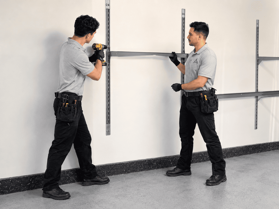 Two workers installing metal wall shelving in a white room, using power tools.
