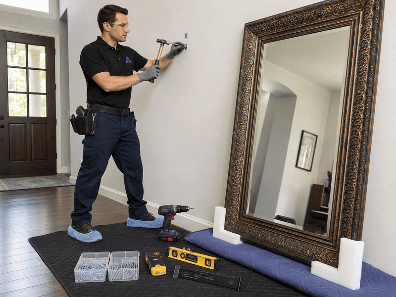 Worker drilling a wall beside a large mirror during home renovation