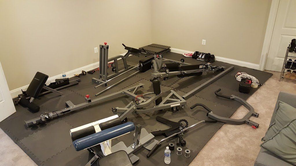 Gym equipment disassembled on a black mat in a room with beige walls.