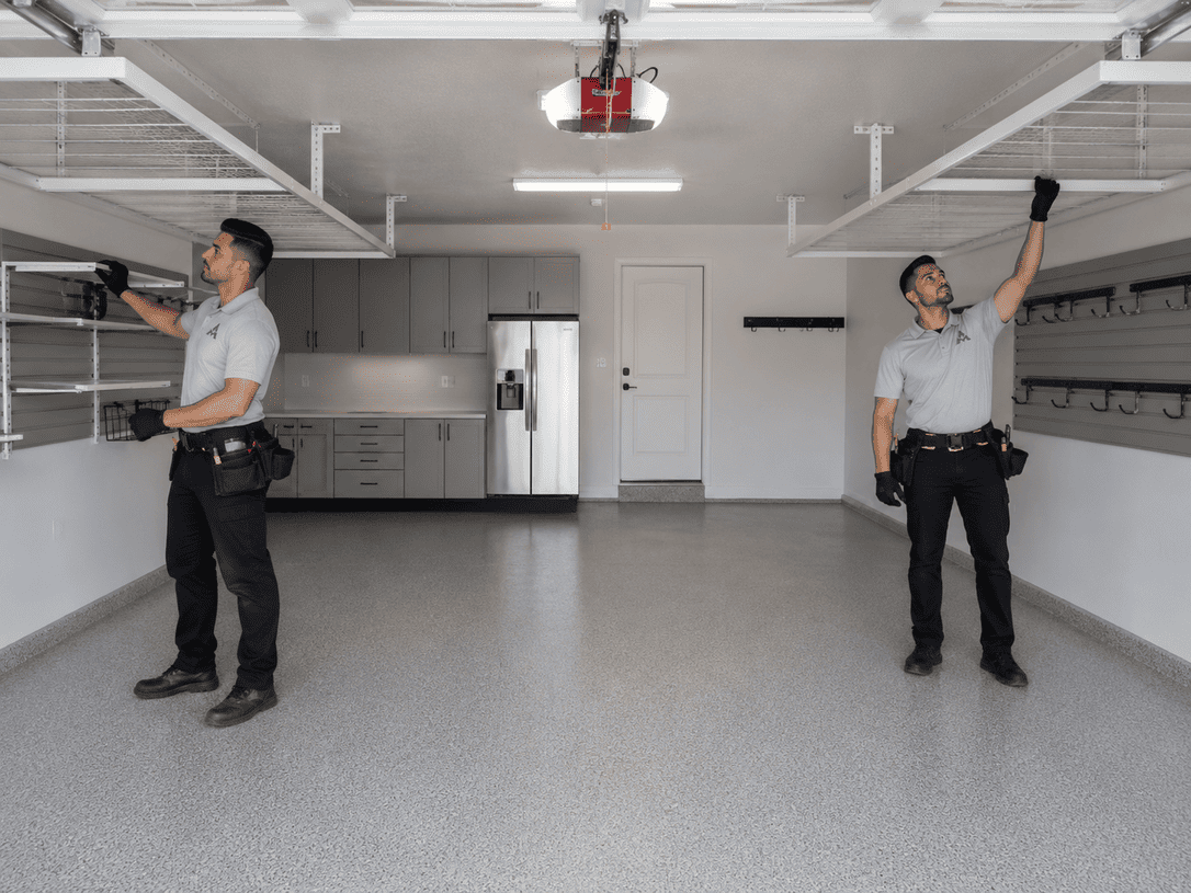 Two technicians in a garage, each holding up a device or tool under a white ceiling.
