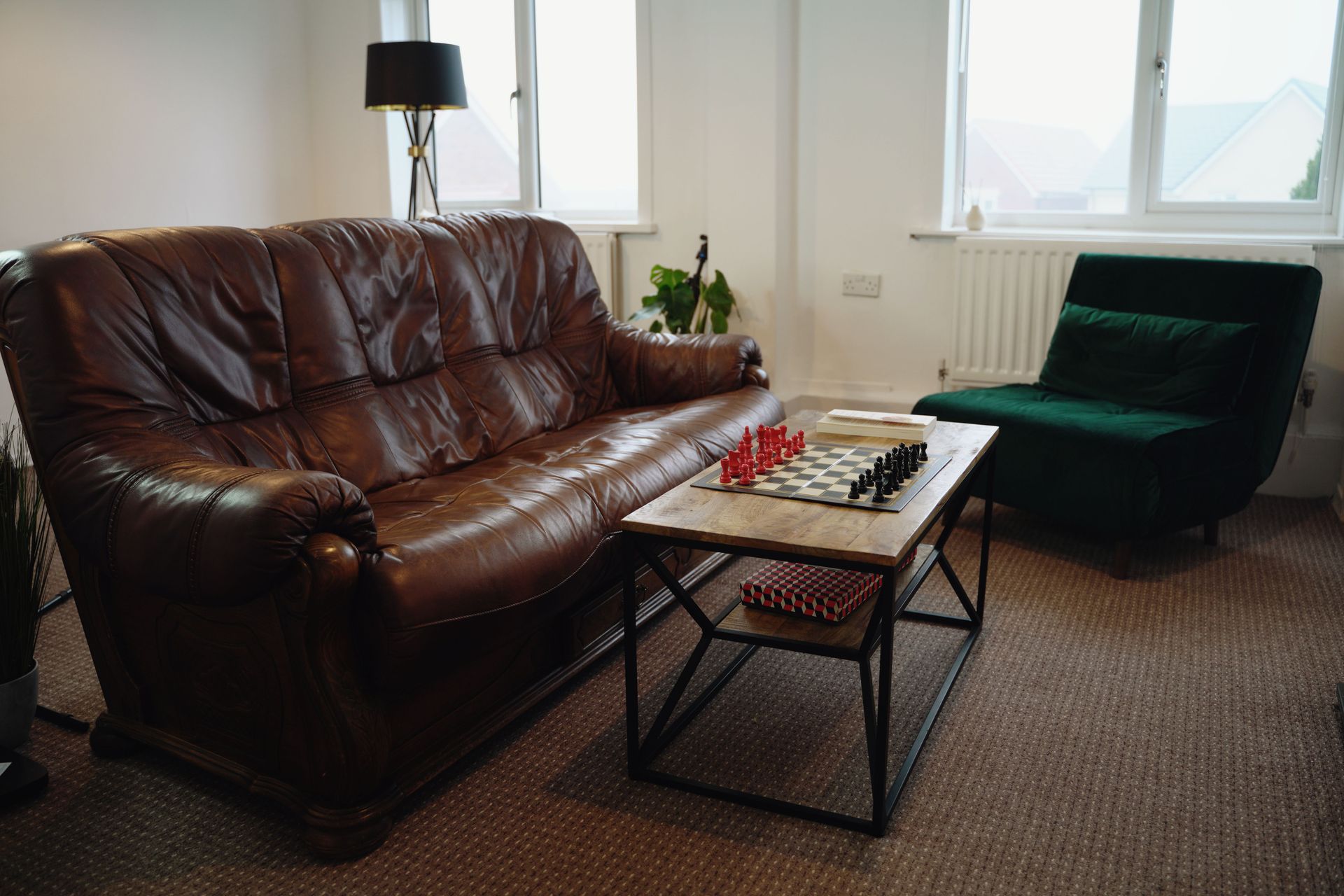 Cozy living room with a brown leather sofa, green armchair, coffee table, and large window