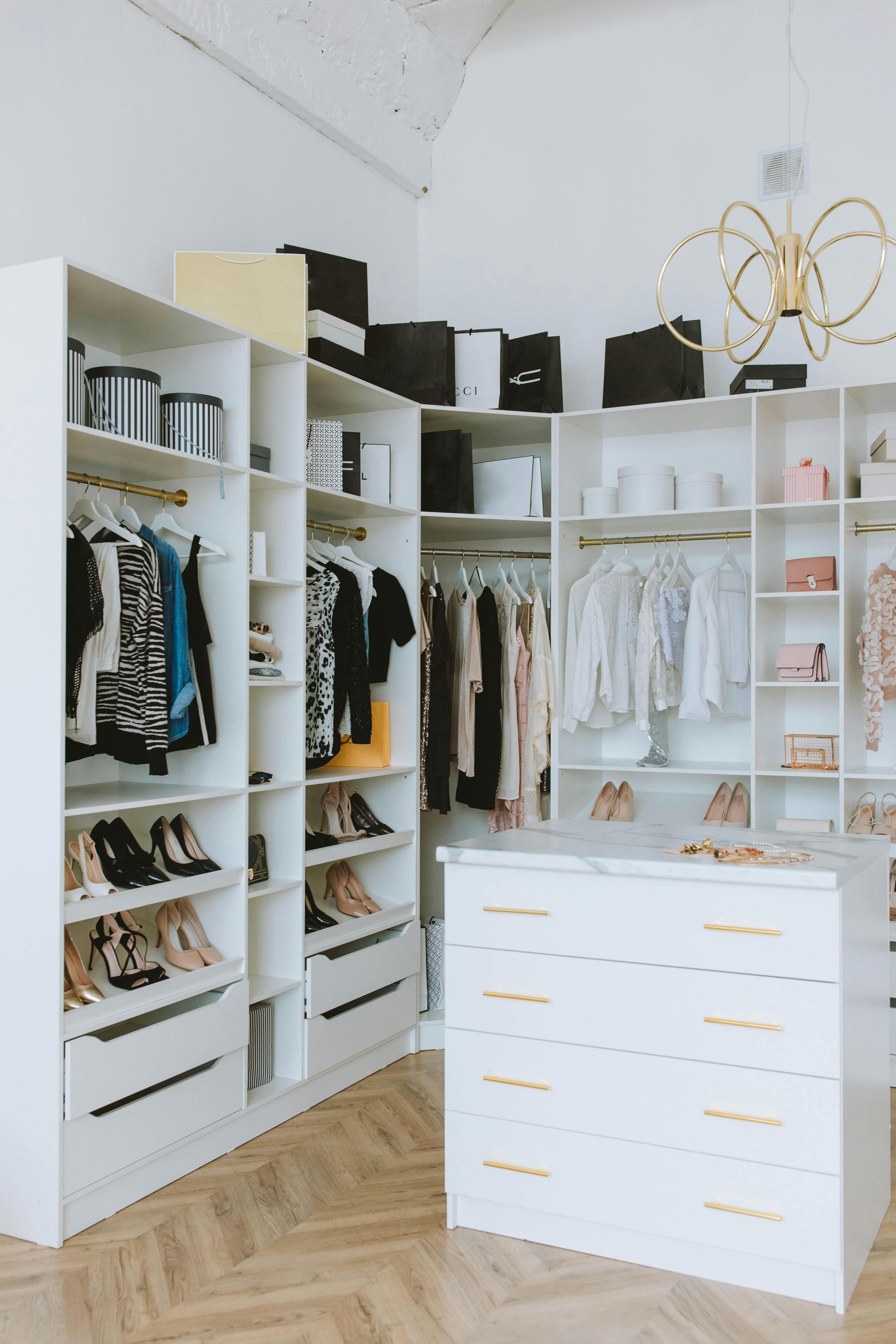 White walk-in closet with organized clothing, shoes, and drawers. A modern, clean design with gold accents.