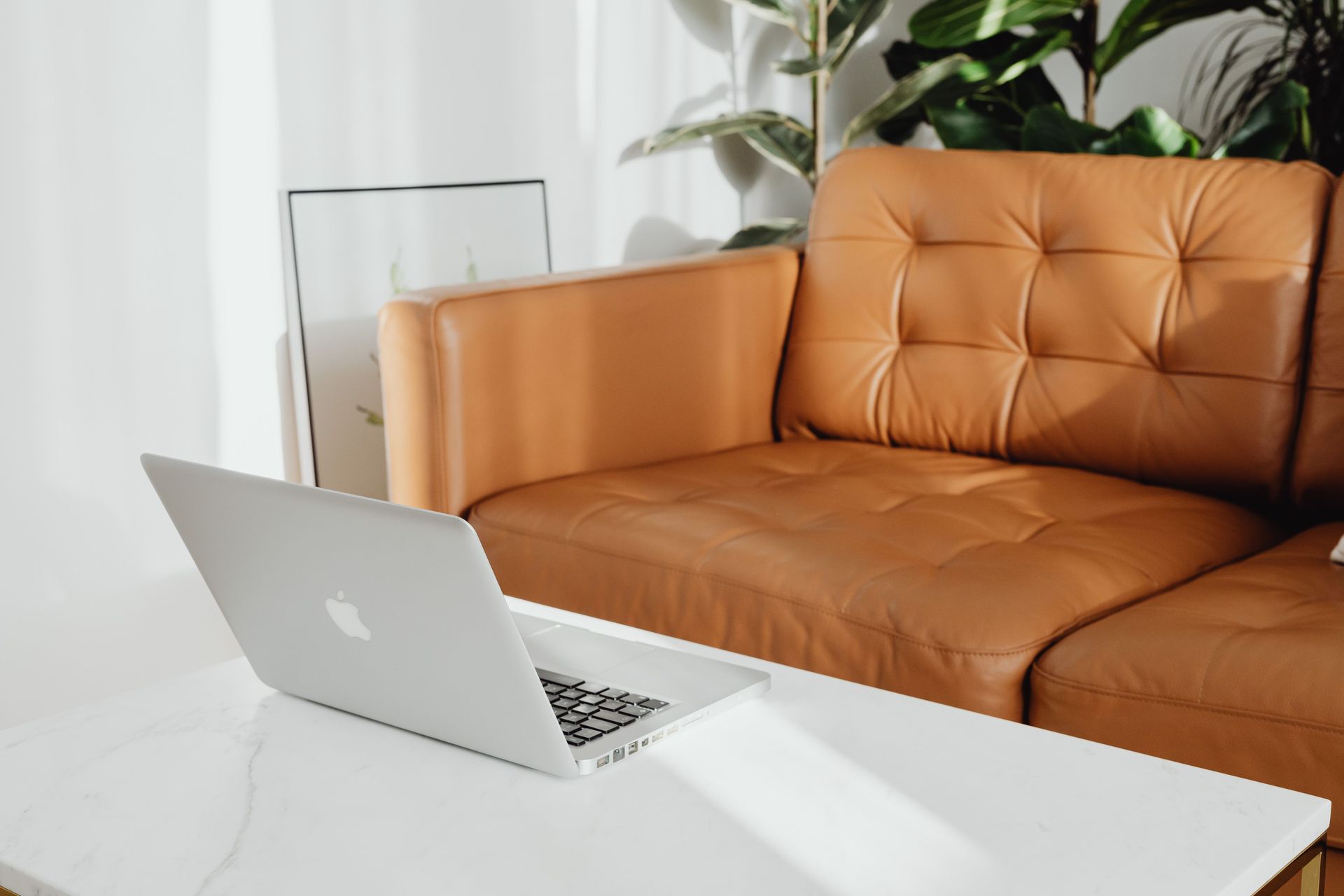 Silver laptop on a white table in front of an orange sofa in a bright living room