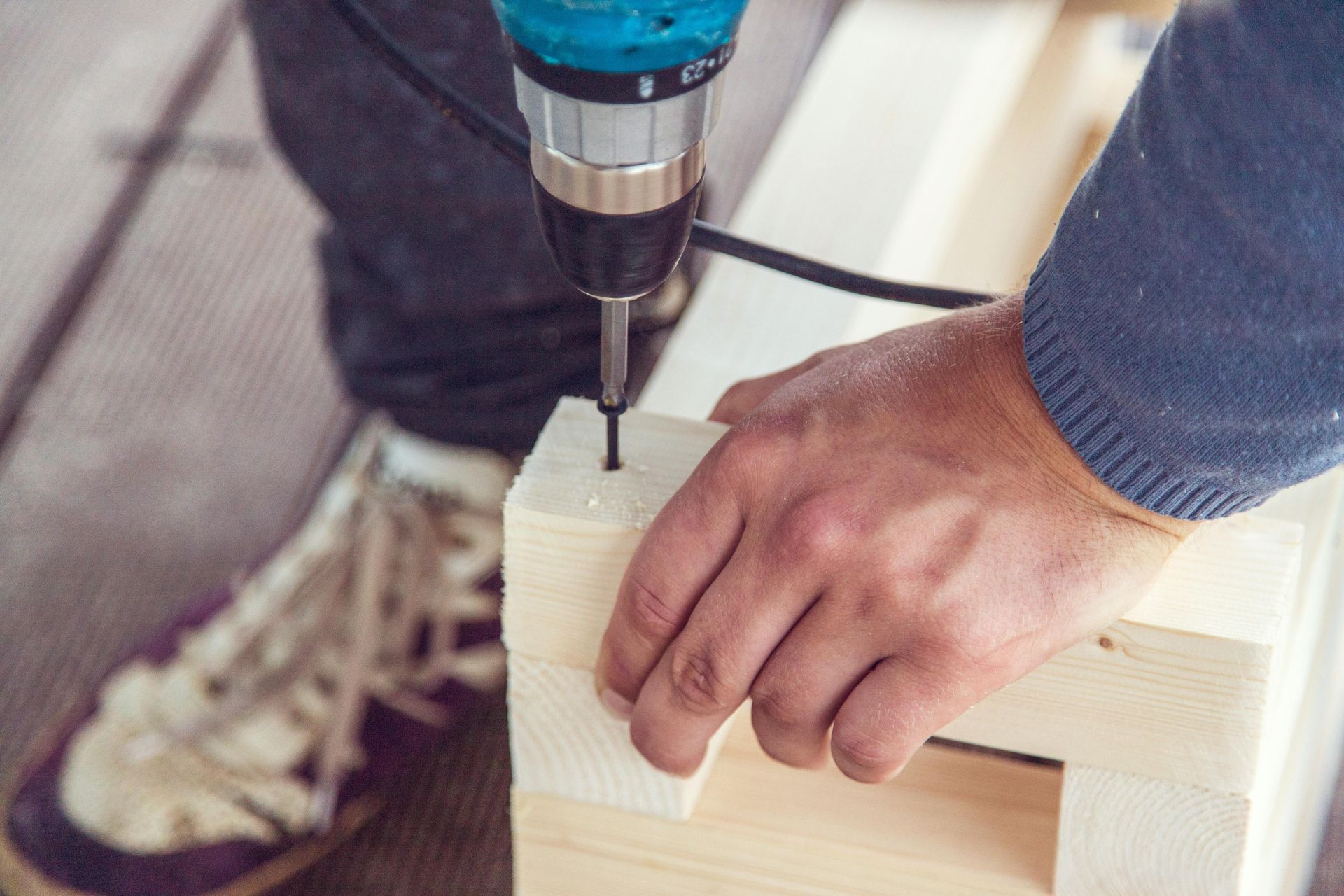 Hand drilling a wooden box with a cordless drill, with a sneakered foot nearby