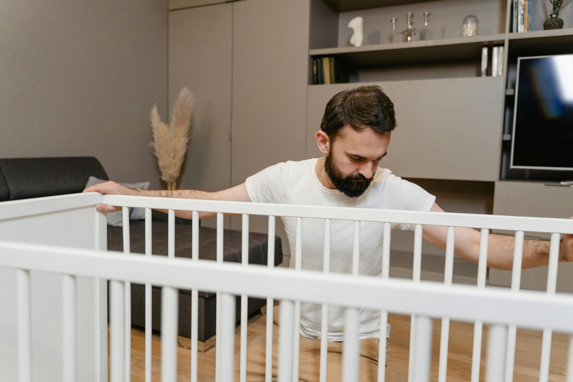 Man leaning into a white crib, looking down in a modern living room