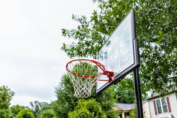 Basketball hoop with clear backboard, red rim, and white net, outdoors.