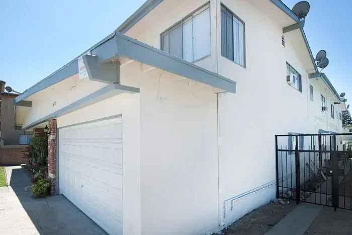 White two-story house with garage and side gate in a sunny residential driveway
