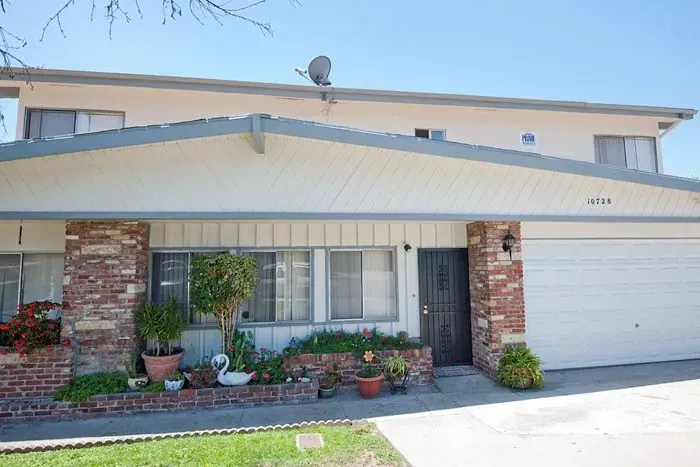 Two-story suburban house with brick pillars, white siding, garage, and small front garden