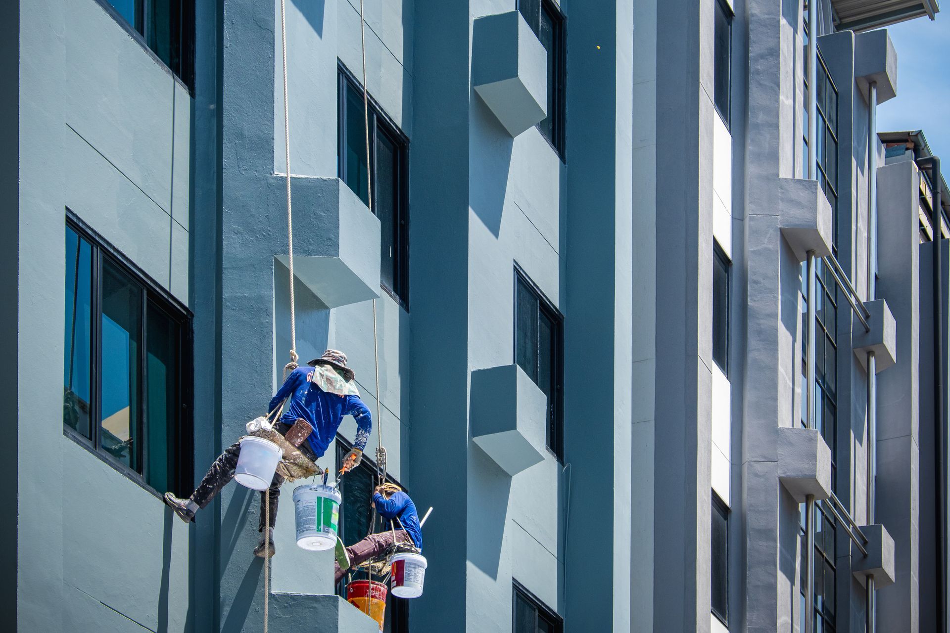 Two window cleaners on ropes working on a tall glass building facade Two window cleaners on ropes working on a tall glass building facade