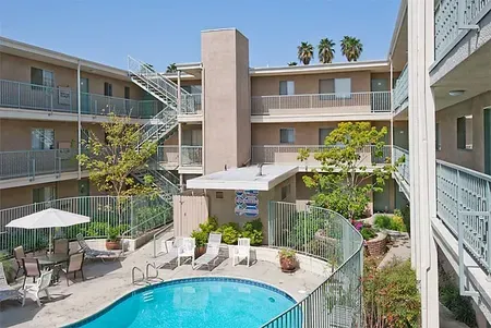 Apartment courtyard with a blue pool, lounge chairs, umbrellas, and multi-story balconies surrounding it Apartment courtyard with a blue pool, lounge chairs, umbrellas, and multi-story balconies surrounding it