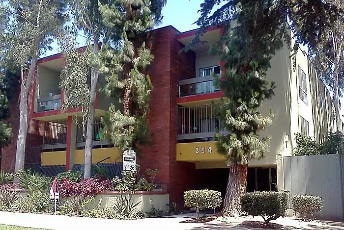 Apartment building with red and yellow balconies, surrounded by tall trees and shrubs.