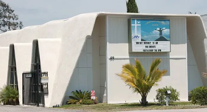 White modern building with a sign, black gates, and a small palm tree out front.