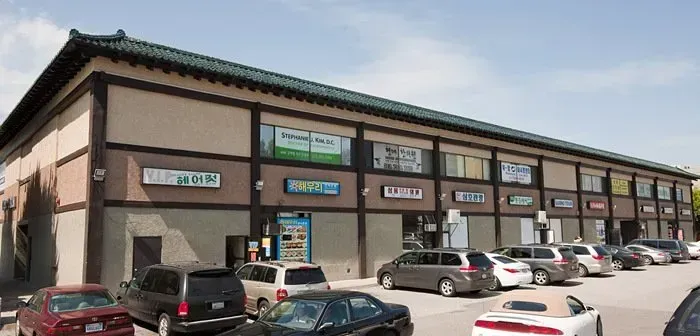 Strip mall storefronts with parked cars along the curb on a sunny day