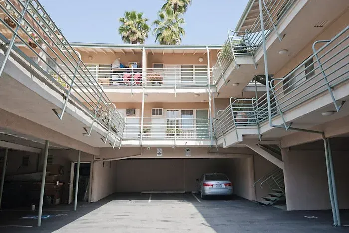 Apartment courtyard with balconies, palm trees, and parked cars in a shaded central area Apartment courtyard with balconies, palm trees, and parked cars in a shaded central area