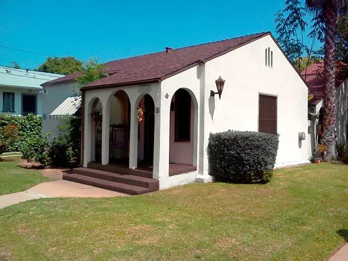 Small white stucco house with arched porch, red roof, and front lawn.