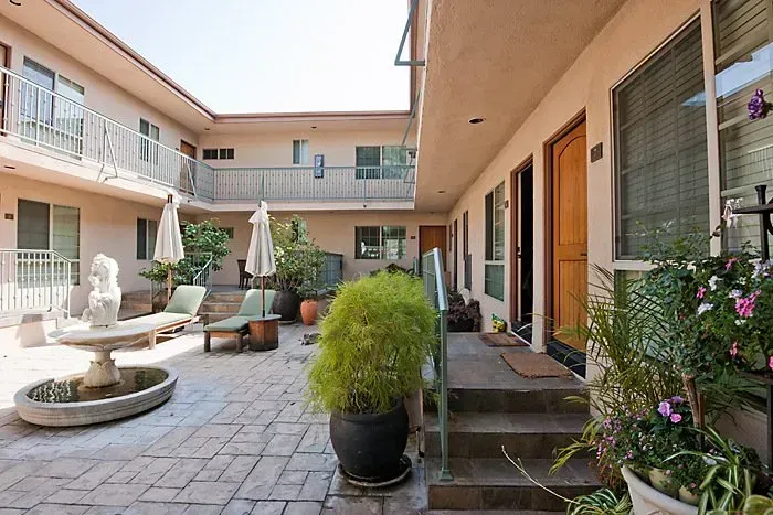 Courtyard patio with potted plants, white chairs, umbrella tables, and apartment doors along the walkway