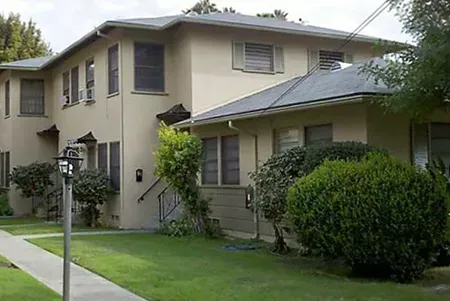 Two-story beige apartment building with a green lawn and bushes along a sidewalk Two-story beige apartment building with a green lawn and bushes along a sidewalk