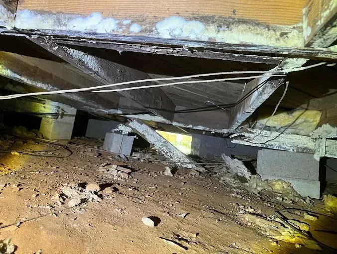Collapsed crawlspace under a floor, with broken beams, debris, and exposed wiring.