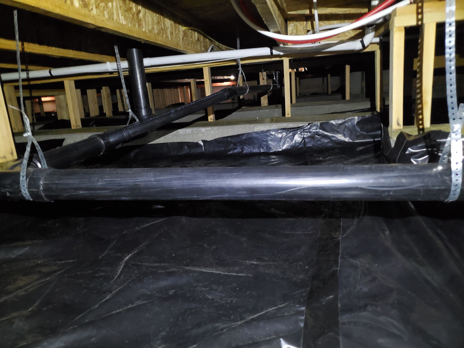 Under-bed view of black plastic sheeting and pipes beneath a raised floor or shelving unit