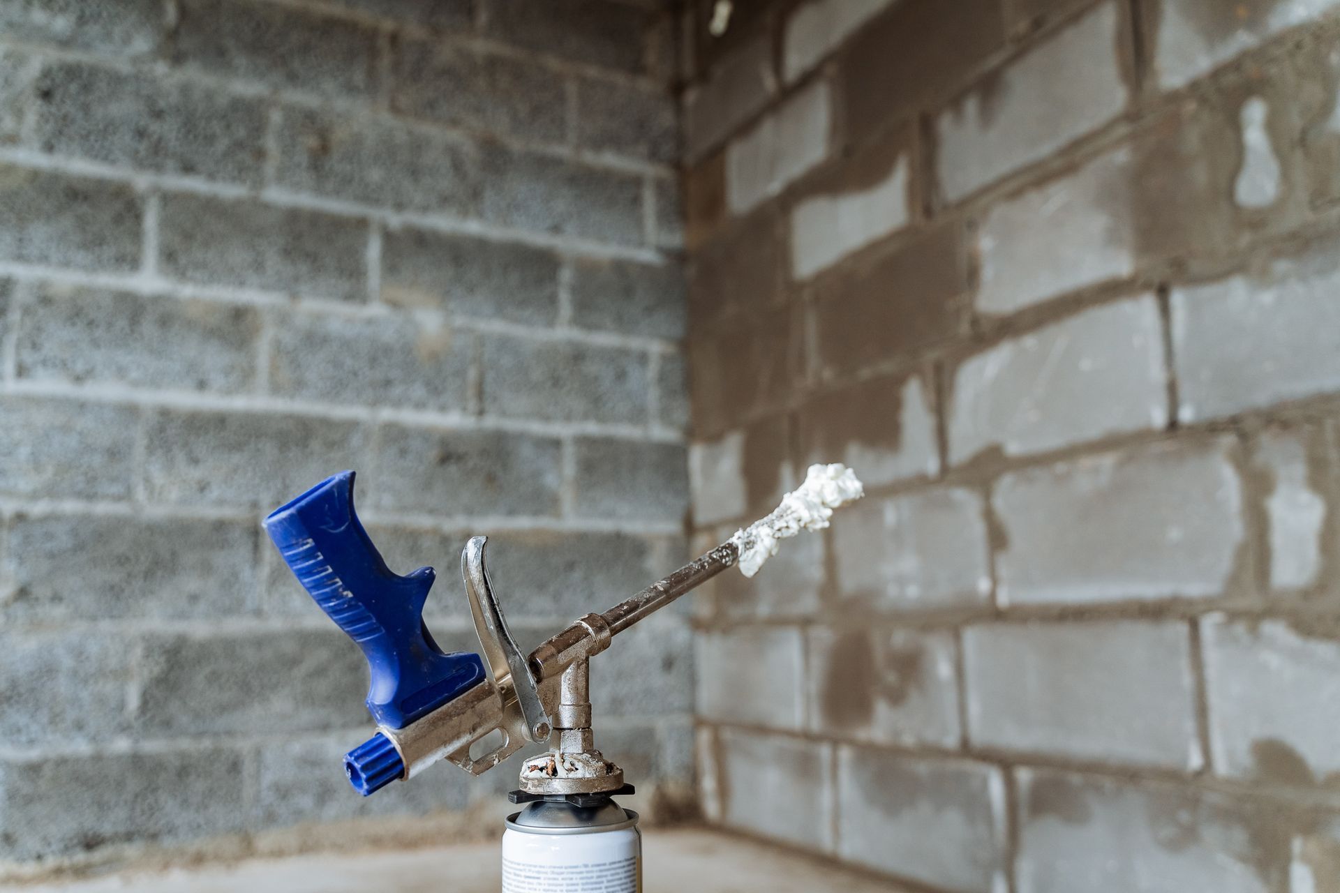 Blue-and-white spray nozzle mounted on a pipe against a cinder block wall
