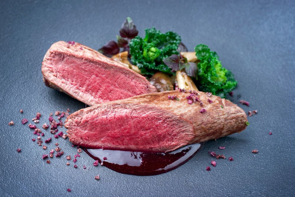 Sliced steak with red center, red wine sauce, and greens on a dark plate — NQ GAME MEAT in Aitkenvale, QLD