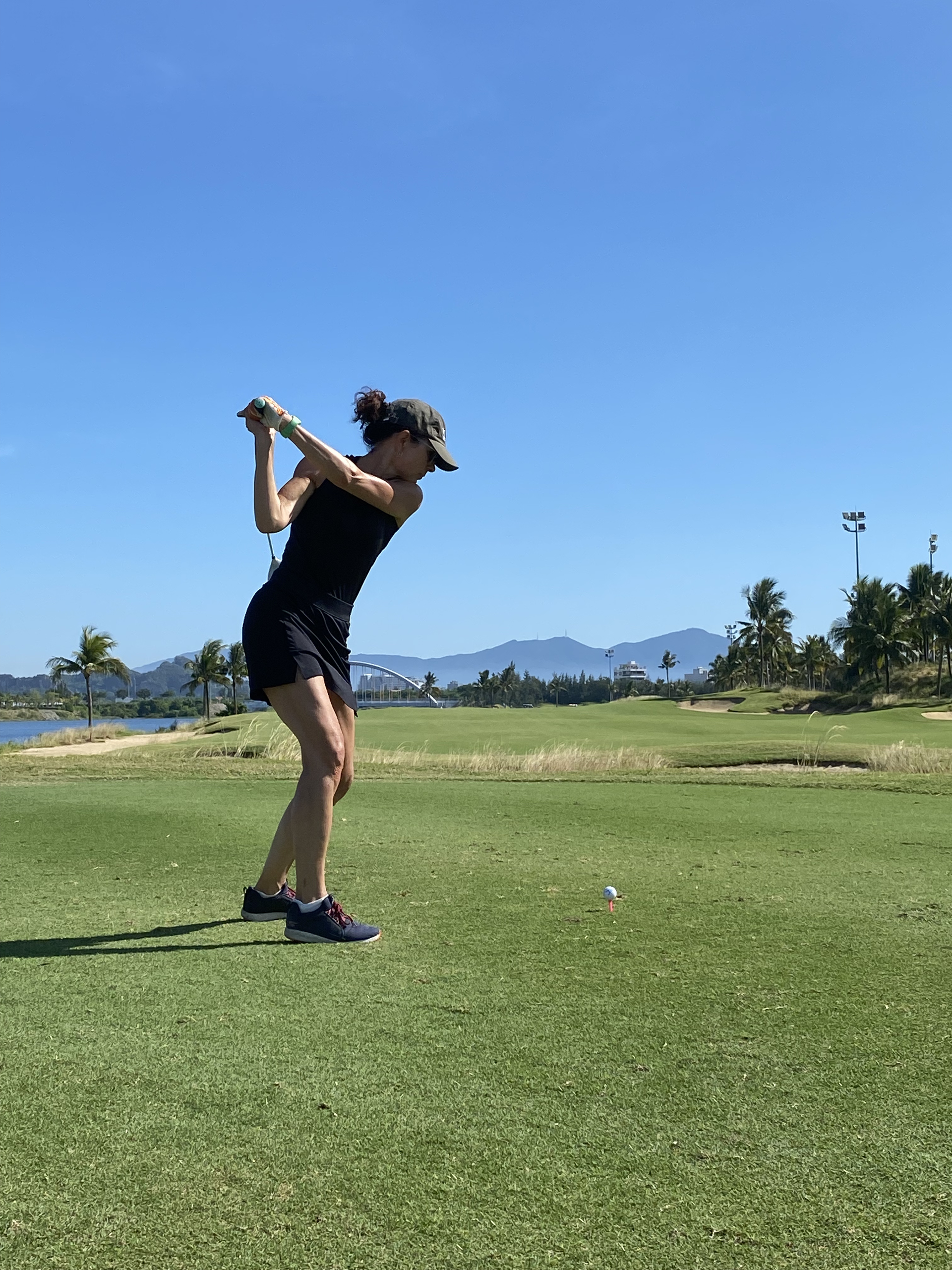 Een golfer zwaait met zijn club op een zonnige, groene golfbaan met bergen in de verte.