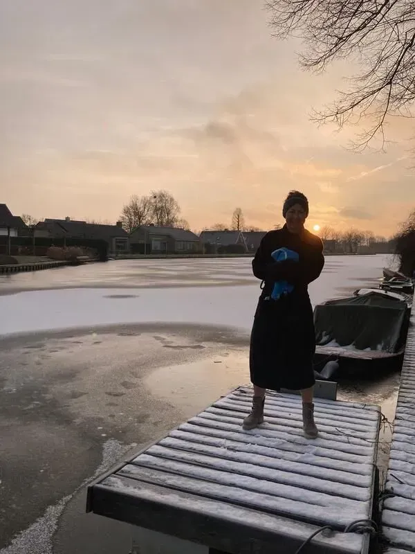 Persoon staat op een besneeuwde steiger bij zonsondergang naast een bevroren meer.