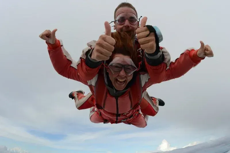 Twee parachutisten in rode overalls steken hun duim omhoog tijdens hun vrije val.