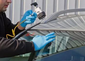 A man wearing blue gloves is fixing a windshield on a car.