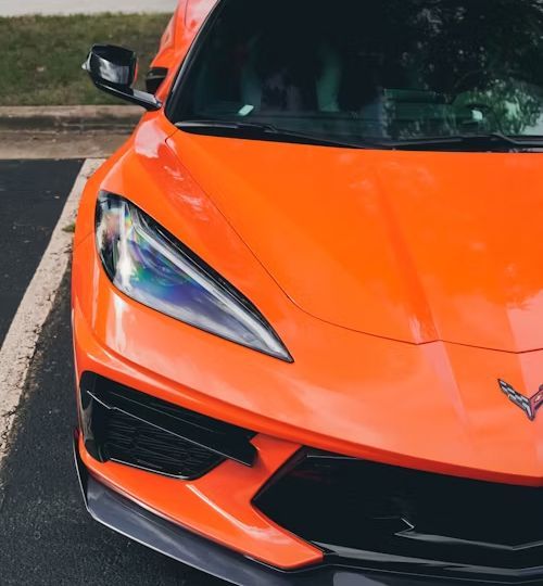 Orange sports car's front end, parked. Black accents on the grill and bumper. The setting is outdoors.