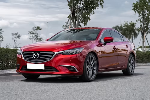 Red Mazda sedan parked on a street under a cloudy sky, front-left view