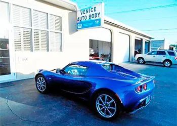 A blue sports car is parked in front of venice auto body