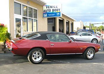 a red car is parked in front of a venice auto body shop .