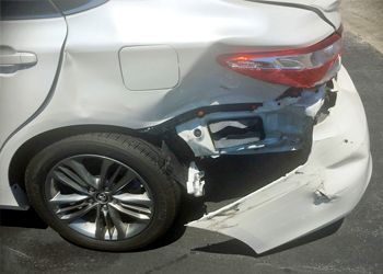 a white car with a damaged bumper is parked on the side of the road .