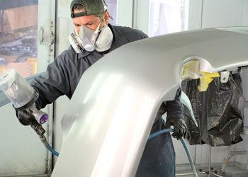 a man wearing a mask is spray painting a car bumper .