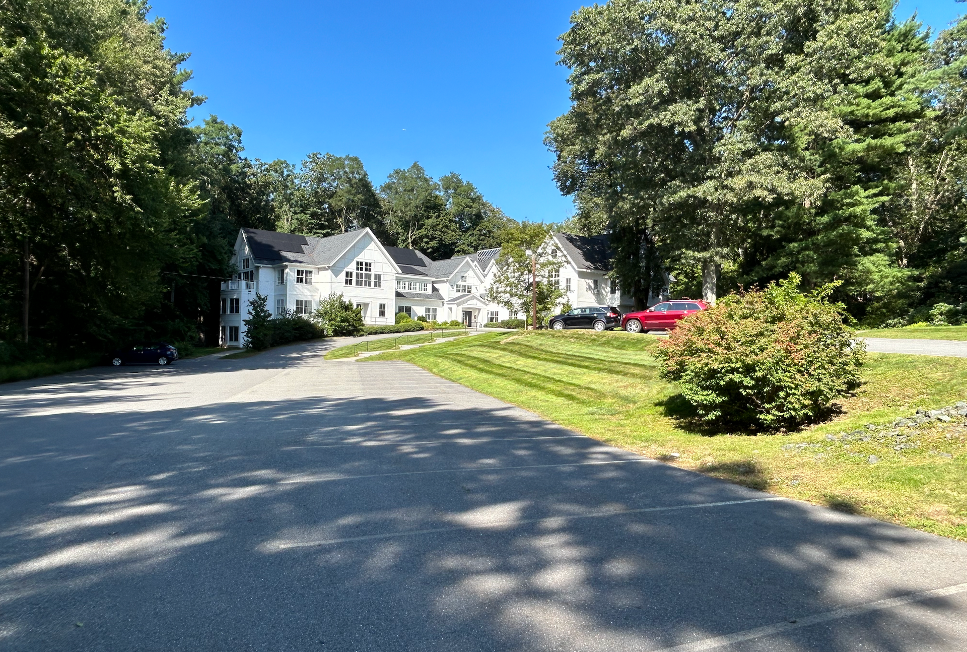 White house surrounded by trees on a sunny day. Paved driveway in front.