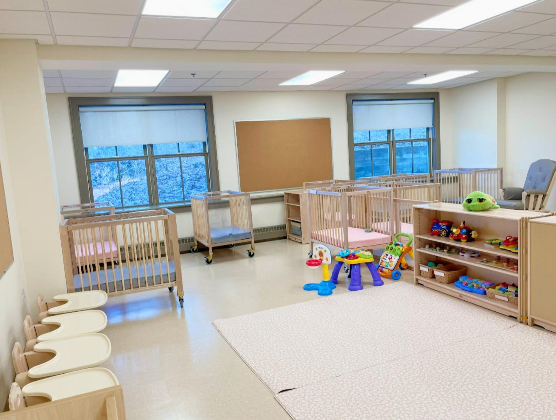 Daycare room with cribs, toys, windows, and a carpet.