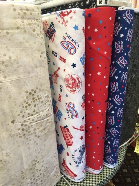 Rolled sports-themed fabric bolts in white, red, and blue displayed on a shelf