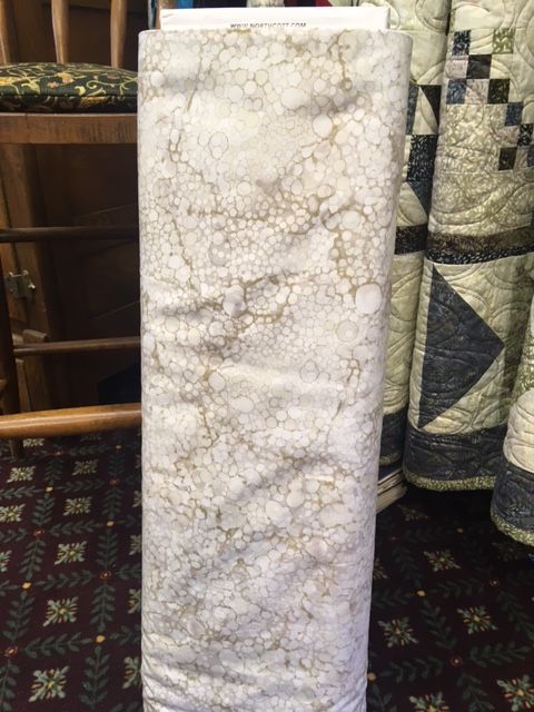 Tall rectangular slab of white and gray veined stone displayed indoors with quilts in the background