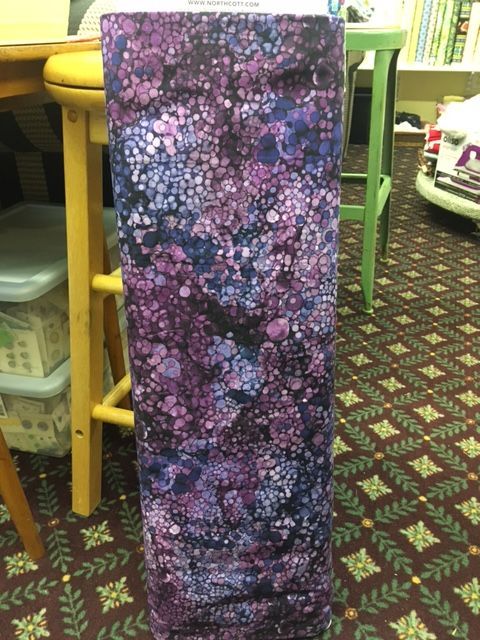 Tall purple-and-black floral foam cushion standing upright in a cluttered room