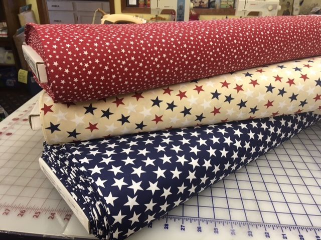 Three rolled fabric bolts with red, cream, and blue star patterns on a cutting table