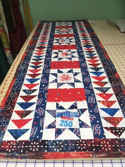 Quilt with red, white, and blue patchwork triangles laid on a bed.